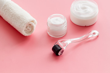 Dermaroller for home cosmetologic procedure near creams on pink background copy space