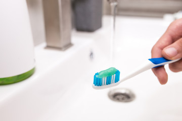 Toothbrush with toothpaste in the guy's hand on the background of the washbasin.