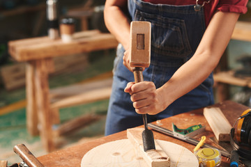 Close-up view of female carpenter striking chisel with hammer into wooden plank for removing wood pieces © DragonImages