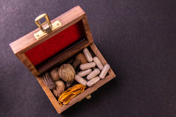 Dried herbs, spices and herbal capsules in a wooden box on black background with copy space. Herbal medicine system concept