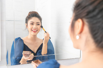 Portrait of a beautiful asian woman as applying makeup near a mirror.