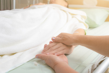 Caring mom holding kind of son hands in bed.