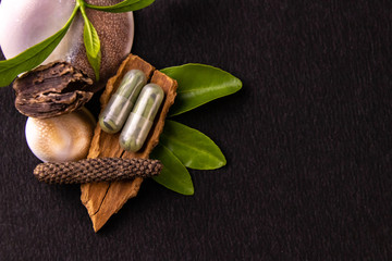 Herbal medicines concept. Ayurvedic capsules with green herbs, whole spices on black background and copy space
