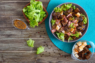 Warm healthy salad of chicken liver, rye croutons, smoked bacon, green salad and mustard sauce in a bowl on a wooden background