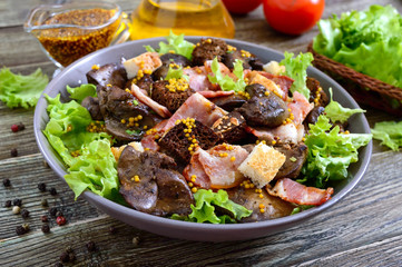 Warm healthy salad of chicken liver, rye croutons, smoked bacon, green salad and mustard sauce in a bowl on a wooden background