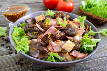 Warm healthy salad of chicken liver, rye croutons, smoked bacon, green salad and mustard sauce in a bowl on a wooden background