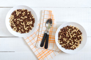 Wholegrain chocolate and milk balls in bowl on white wooden background. Healthy cereal breakfast. Baby breakfast. Baby eating. Balanced diet.