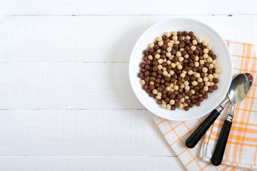 Wholegrain chocolate and milk balls in bowl on white wooden background. Healthy cereal breakfast. Baby breakfast. Baby eating. Balanced diet. Copy space