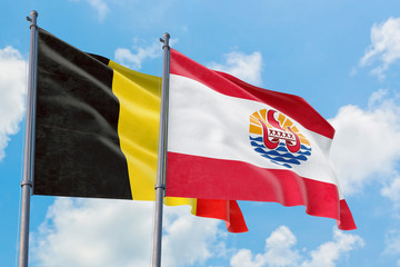 French Polynesia and Belgium flags waving in the wind against white cloudy blue sky together. Diplomacy concept, international relations.