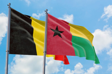 Guinea Bissau and Belgium flags waving in the wind against white cloudy blue sky together. Diplomacy concept, international relations.