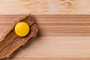 One yellow tablet pill placed on an inverted cinnamon stick with unique textured background. Herbal medicine concept