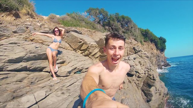 POV shot of Young Man Cliff Jumping and Lifestyle Woman Dancing in Background on Rocks. Action Camera Shot Footage 120 fps Slow Motion. Happy people Have a Fun 
