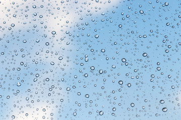 Fototapeta na wymiar beautiful raindrops on glass window while raining with different texture with blue color blurred background.