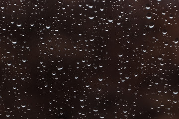 beautiful raindrops on glass window while raining with different texture with dark color blurred background.