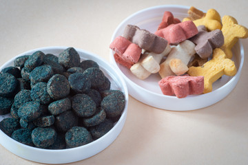 Dog treats and spirulina for pets, in small bowls, pale background.