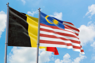 Malaysia and Belgium flags waving in the wind against white cloudy blue sky together. Diplomacy concept, international relations.