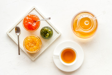 Fruit jam near tea on white kitchen desk flat lay