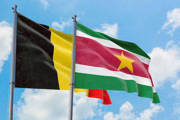 Suriname and Belgium flags waving in the wind against white cloudy blue sky together. Diplomacy concept, international relations.