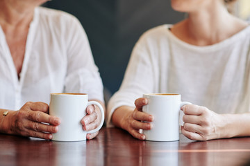 Cropped image of mature woman and her adult daughter drinking coffee and discussing news and...