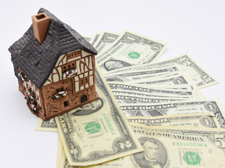 The ceramic house stands on dollars, on a light background.