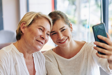 Smiling mother and daughter taking selfie on smartphone in cafe on Mothers day