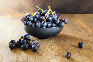 Bunch of black grapes in a bowl on wooden background.