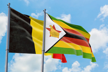 Zimbabwe and Belgium flags waving in the wind against white cloudy blue sky together. Diplomacy concept, international relations.