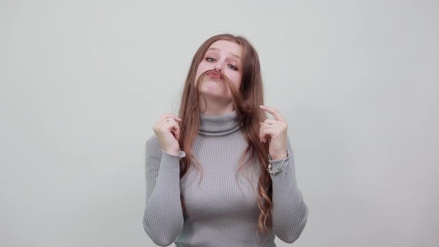 young beautiful red haired woman in gray sweater made her hair an imitation of man's moustache with silly and funny expression on face