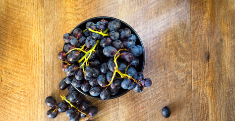 Black grapes in a bowl on warm wooden background.