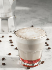 Hot coffee cappuccino with raspberry syrup in glass with milk foam on table. Coffee beans on the table. Shallow depth of field, focus on the cup. Close up.