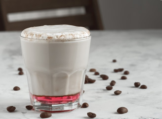 Hot coffee cappuccino with raspberry syrup in glass with milk foam on table. Coffee beans on the table. Shallow depth of field, focus on the cup. Close up. Copy space.