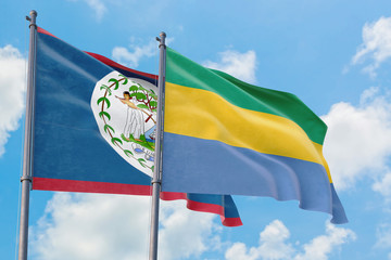 Gabon and Belize flags waving in the wind against white cloudy blue sky together. Diplomacy...