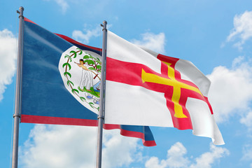 Guernsey and Belize flags waving in the wind against white cloudy blue sky together. Diplomacy...