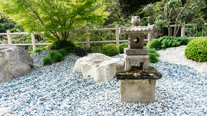 A picturesque photography of a Japanese-style stone garden with colorful pebbles, boulders, tachi gata lantern, trimmed boxwood bushes and maples. Garden with landscaping in traditional Japanese style