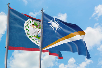 Marshall Islands and Belize flags waving in the wind against white cloudy blue sky together....