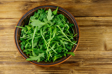 Obraz na płótnie Canvas Fresh green arugula in ceramic bowl on a wooden table. Top view. Healthy food or vegetarian concept