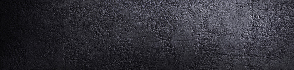 Black grunge background. The texture of the concrete wall closeup. Rough surface in reflection of light. Dark gray grunge banner with copy space for your design.
