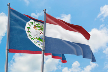 Netherlands and Belize flags waving in the wind against white cloudy blue sky together. Diplomacy concept, international relations.
