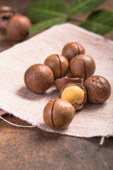 Pile macadamia nuts open kernels and shells in burlap bag on wooden background
