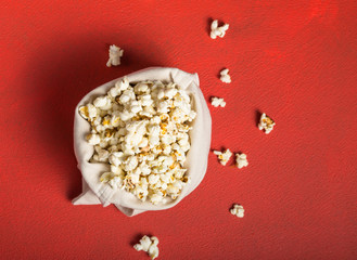 Fresh popcorn spilled out of the  bag on a red background. Cinema snack concept. The food for watching a movie and entertainment. Copy space for text, flat lay.