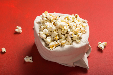 Fresh popcorn spilled out of the  bag on a red background. Cinema snack concept. The food for watching a movie and entertainment. Copy space for text, flat lay.