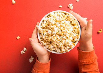 Popcorn viewed from above on red background. Child eating popcorn. Human hand.  Cinema snack concept. The food for watching a movie and entertainment. Copy space for text, flat lay.