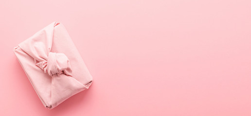 Holiday gift wrapped in cloth in the style of Furoshiki on a pink background. Zero Waste Life Holiday Concept.