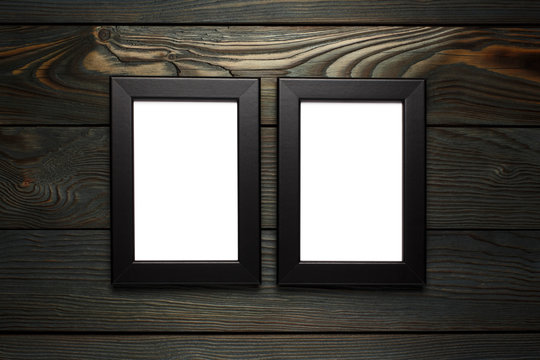 Two black empty frames hanging on the dark wooden wall