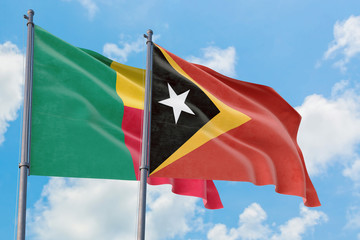 East Timor and Benin flags waving in the wind against white cloudy blue sky together. Diplomacy concept, international relations.