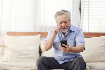 Older men move glasses down to look at the phone in the hand due to Hyperopia problems, which makes vision difficult.Health problems of the elderly.