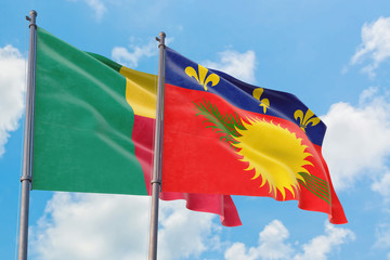 Guadeloupe and Benin flags waving in the wind against white cloudy blue sky together. Diplomacy concept, international relations.