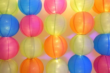 In selective focus a row of multicolored Chinese lanterns hanging on a wire with white wall background 