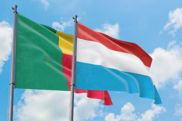 Fototapeta na wymiar Luxembourg and Benin flags waving in the wind against white cloudy blue sky together. Diplomacy concept, international relations.