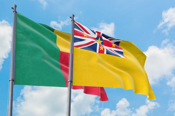Niue and Benin flags waving in the wind against white cloudy blue sky together. Diplomacy concept,...